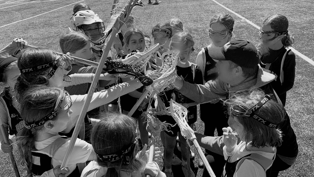 Youth lacrosse team huddle with coach